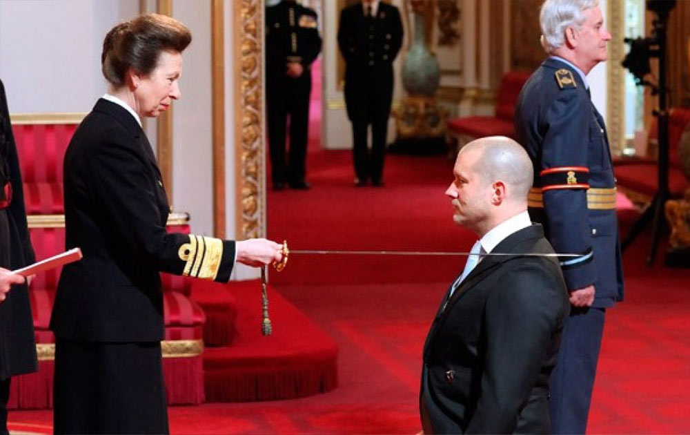 Jony Ive kneels to be knighted by the Princess Royal at Buckingham Palace